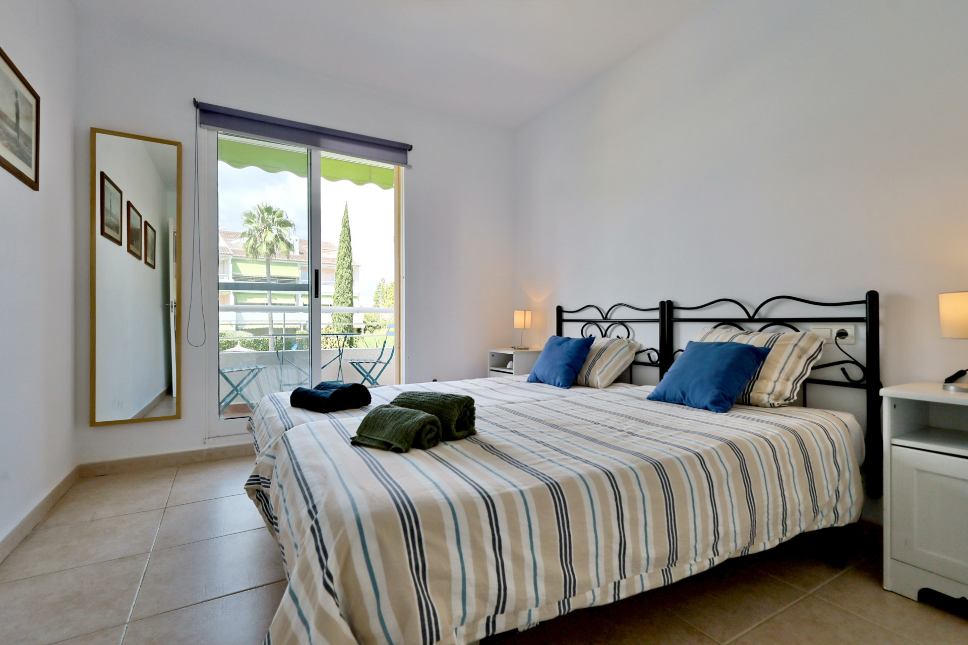 Chambre lumineuse avec lits jumeaux, têtes de lit en fer forgé et porte coulissante donnant sur un balcon privé avec vue.