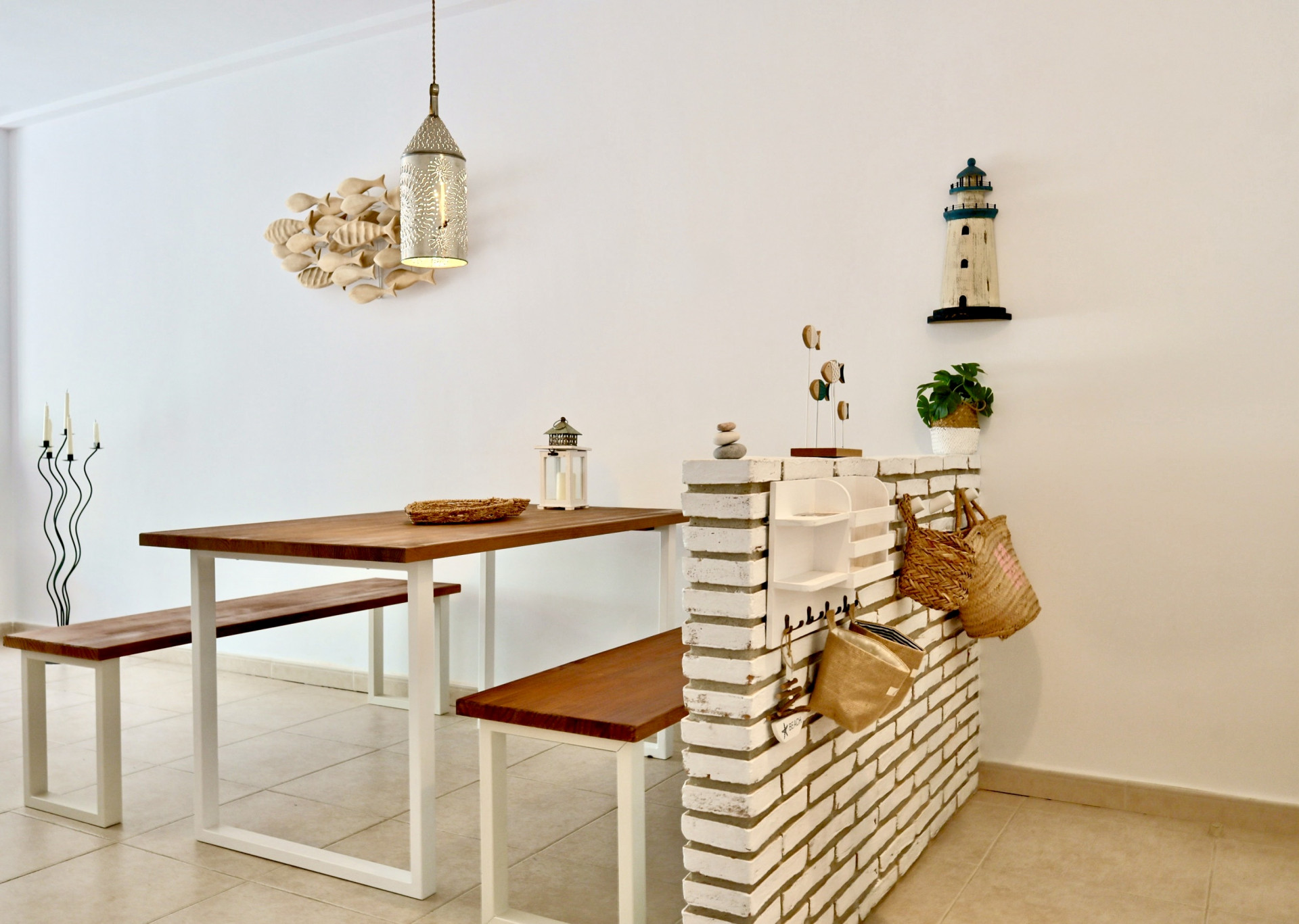 Coin repas comprenant une table et des bancs en bois massif sur pieds blancs, séparé par un muret en briques blanches avec une décoration nautique.