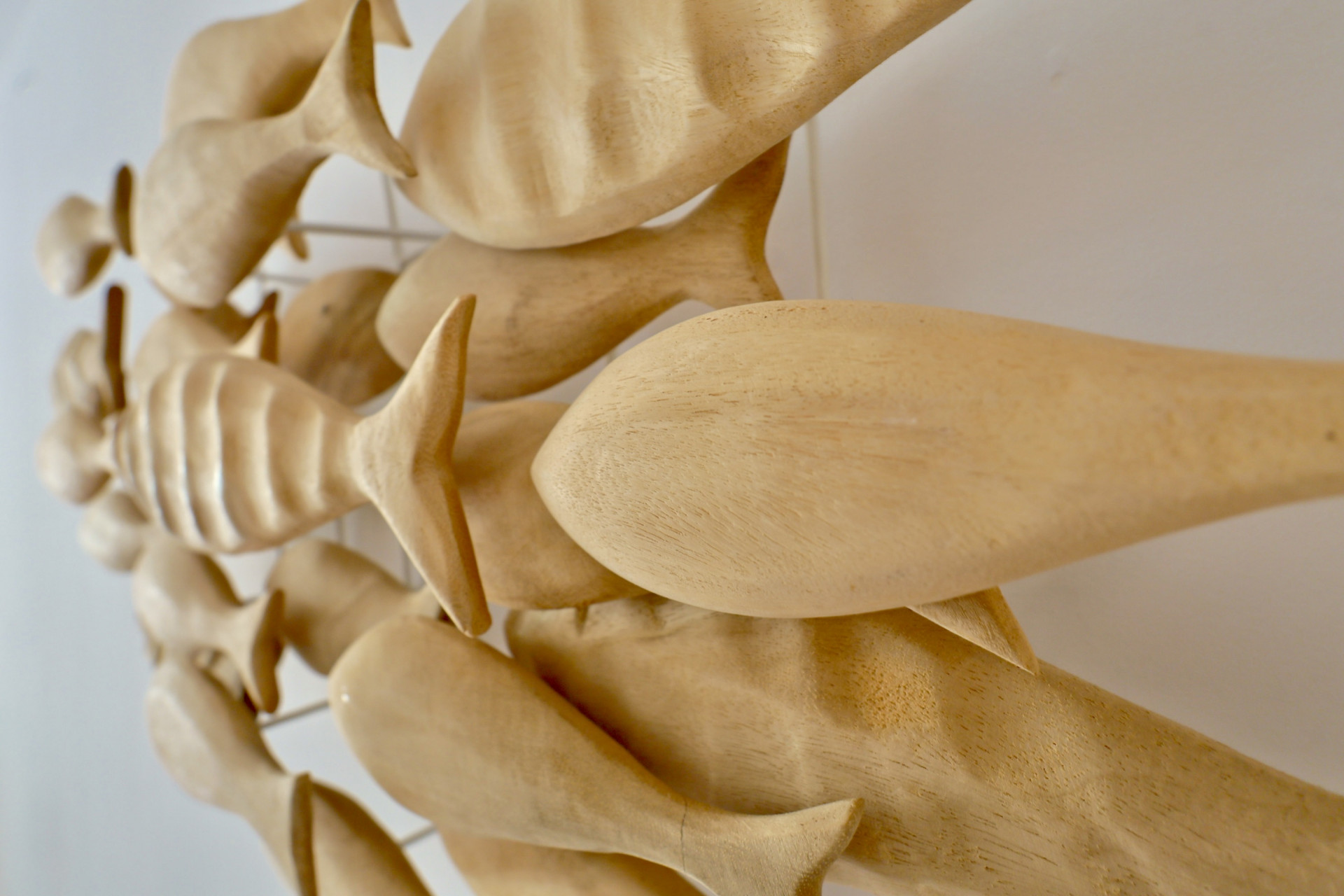 Gros plan d'une sculpture murale décorative représentant des poissons en bois sculptés à la main, fixés sur un support métallique discret sur un mur blanc.