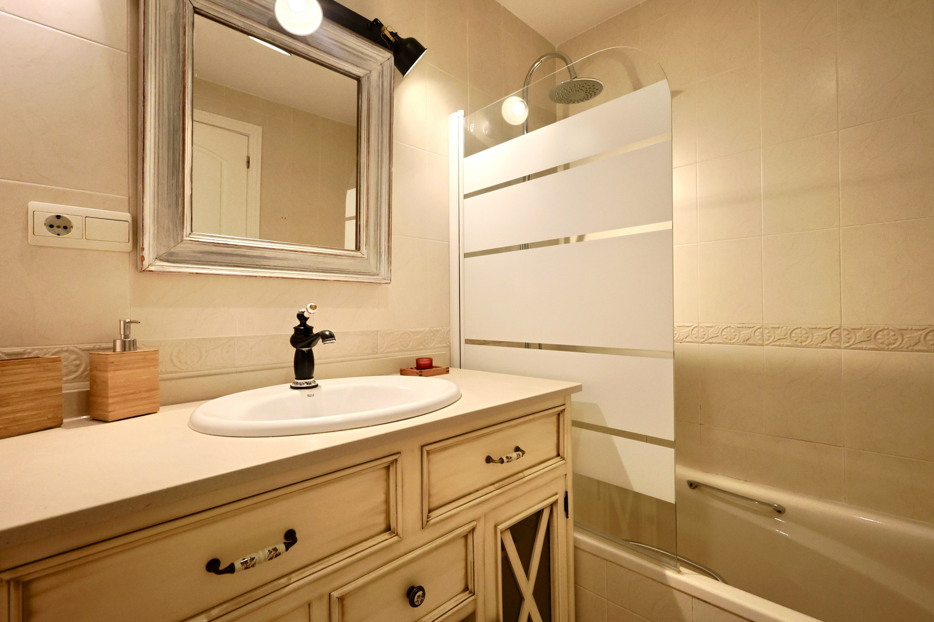 Salle de bain avec meuble vasque de style vintage, robinetterie noire, miroir encadré et baignoire avec pare-douche sérigraphié.