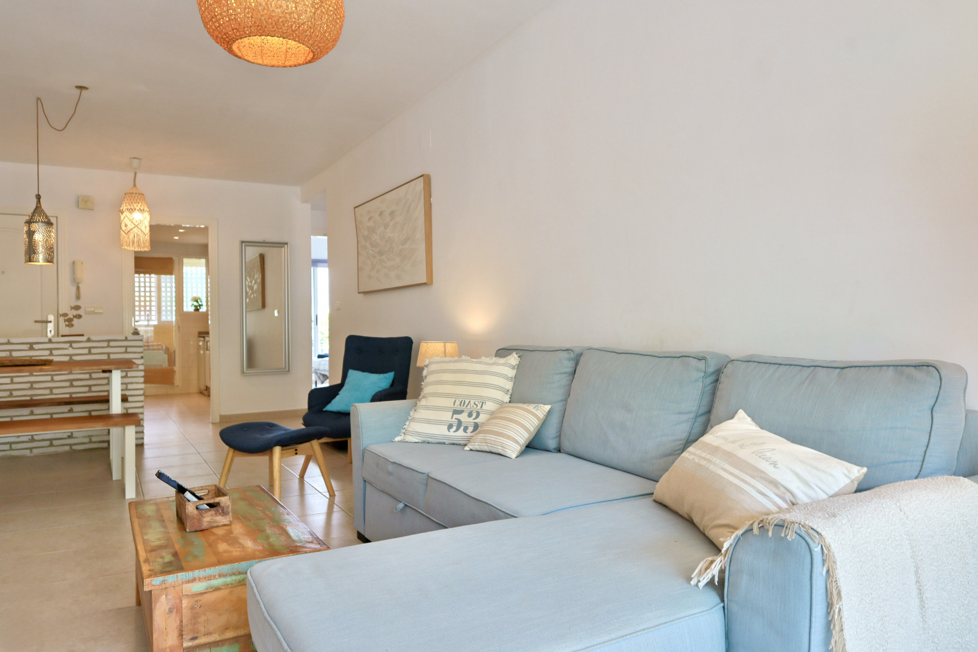 Salon ouvert comprenant un canapé d'angle bleu clair, une table basse en bois rustique et un coin repas avec des accents de brique et des suspensions tressées.