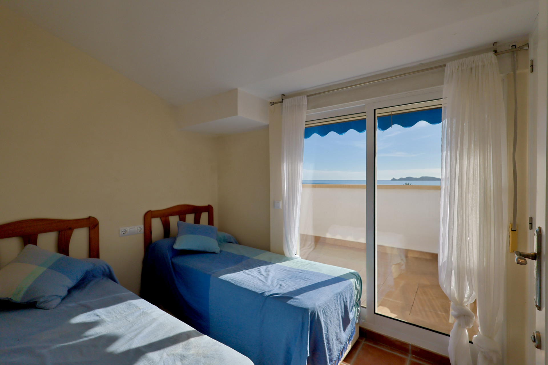 Chambre avec deux lits simples, têtes de lit en bois et accès direct à une terrasse offrant une vue panoramique sur la mer.