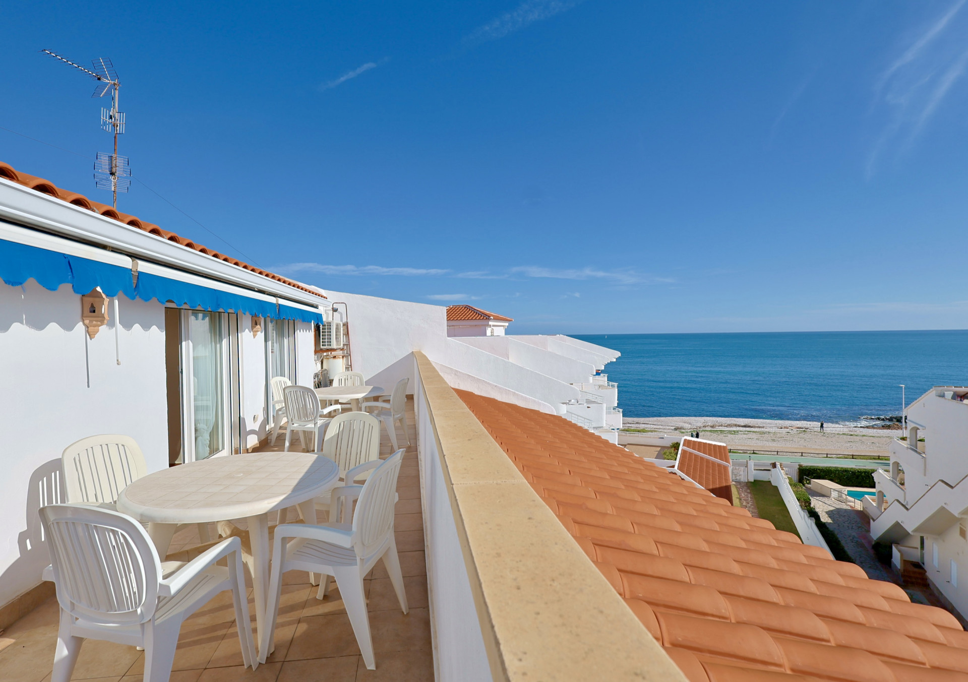 Terrasse en première ligne avec vue sur la mer, comprenant un mobilier d'extérieur blanc, un store bleu et une vue directe sur la plage de galets.