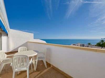 Grande terrasse avec mobilier de jardin blanc et carrelage clair, offrant une vue imprenable sur la mer Méditerranée et un ciel azur. Une avancée de terre se distingue au loin.
