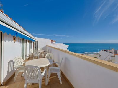 Grande terrasse privée avec mobilier de jardin blanc, store bleu et vues panoramiques sur la mer Méditerranée sous un ciel clair.