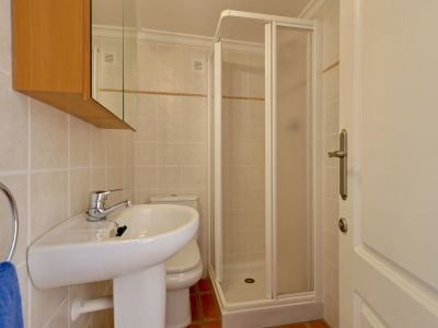 Salle de bain compacte avec lavabo sur pied, toilettes et cabine de douche d'angle. Carrelage mural clair avec frise décorative et sol en terre cuite.