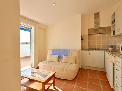 Séjour-cuisine ouvert avec canapé et table basse en bois. Sol carrelé en terre cuite, cuisine équipée d'une hotte et d'un plan de travail en granit, et accès terrasse.