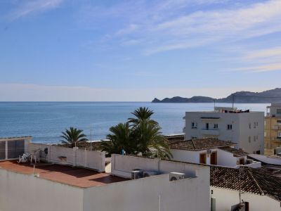 Vue panoramique sur la Méditerranée depuis la propriété, avec la mer bleue, des toits en terre cuite et des palmiers, et la côte montagneuse au loin.