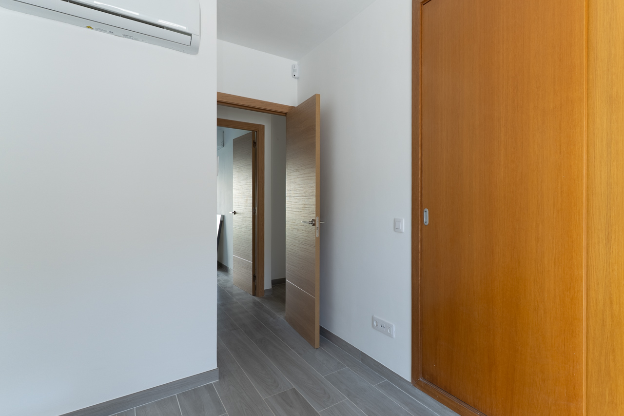 Couloir moderne avec portes en bois, placard intégré, carrelage gris effet bois et unité de climatisation murale sur mur blanc.