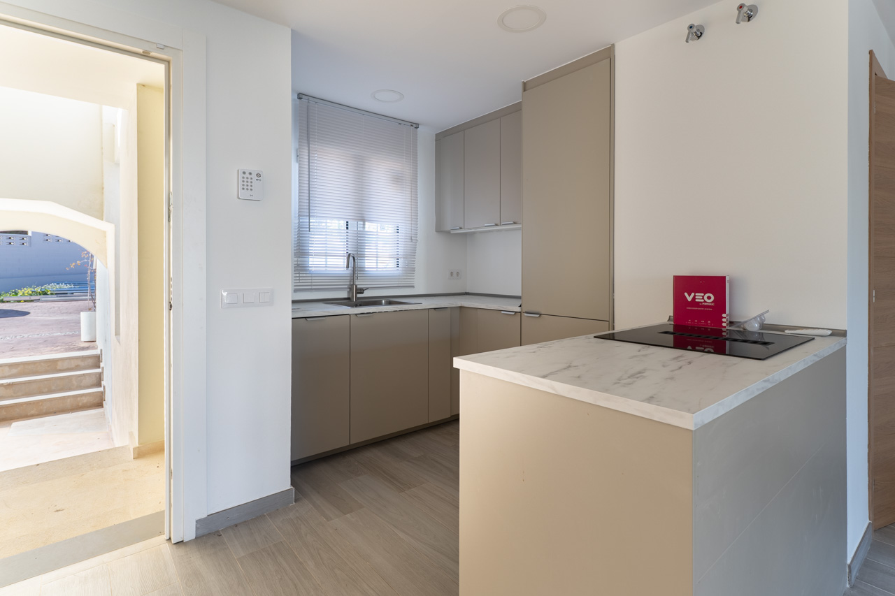 Cuisine moderne avec meubles taupe, plans de travail effet marbre et plaque à induction. Une fenêtre avec stores apporte de la lumière sur l'évier en inox.