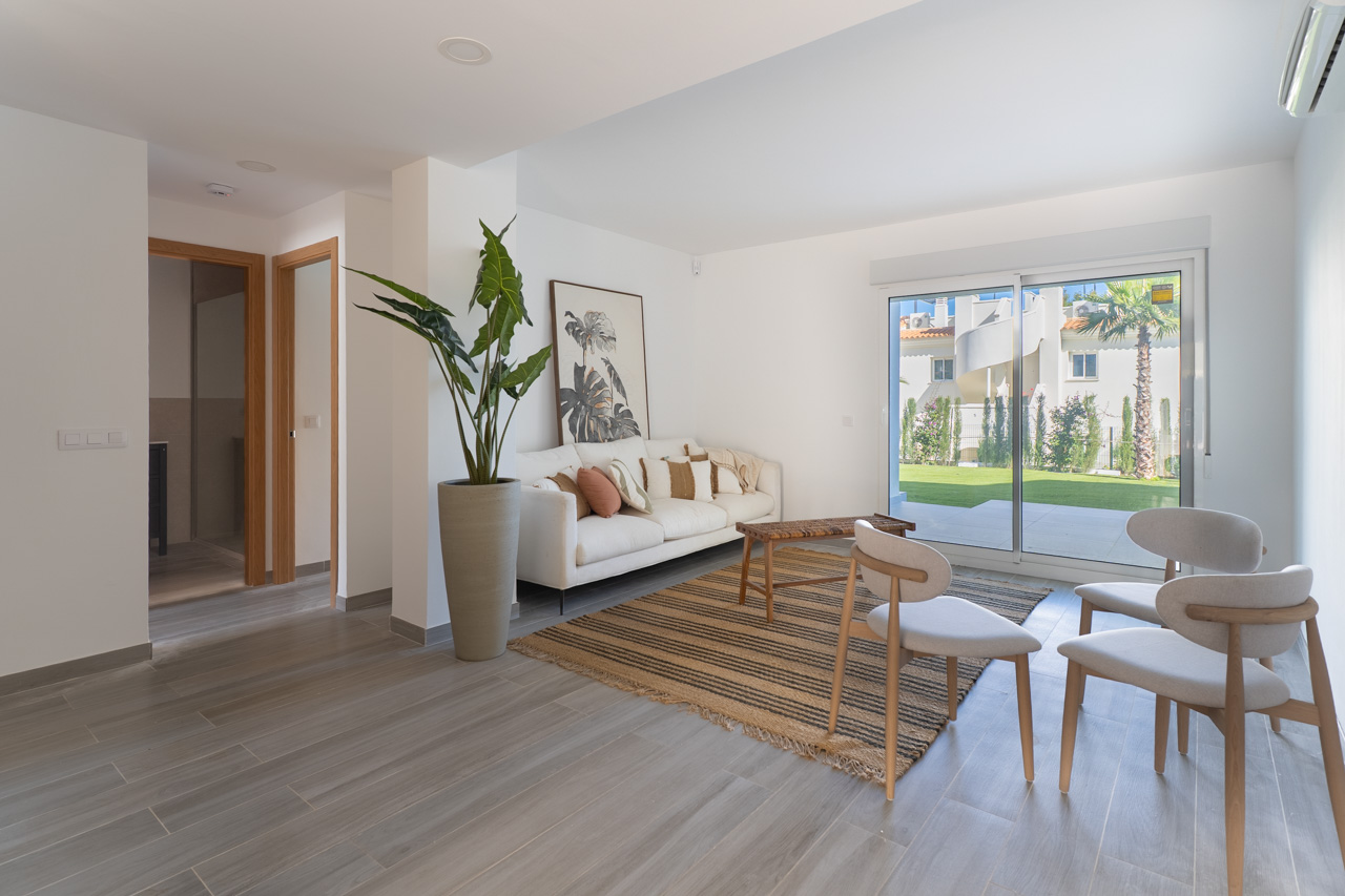 Espace de vie moderne avec sol en grès cérame gris, canapé blanc et grandes baies vitrées ouvrant sur un jardin privatif verdoyant.