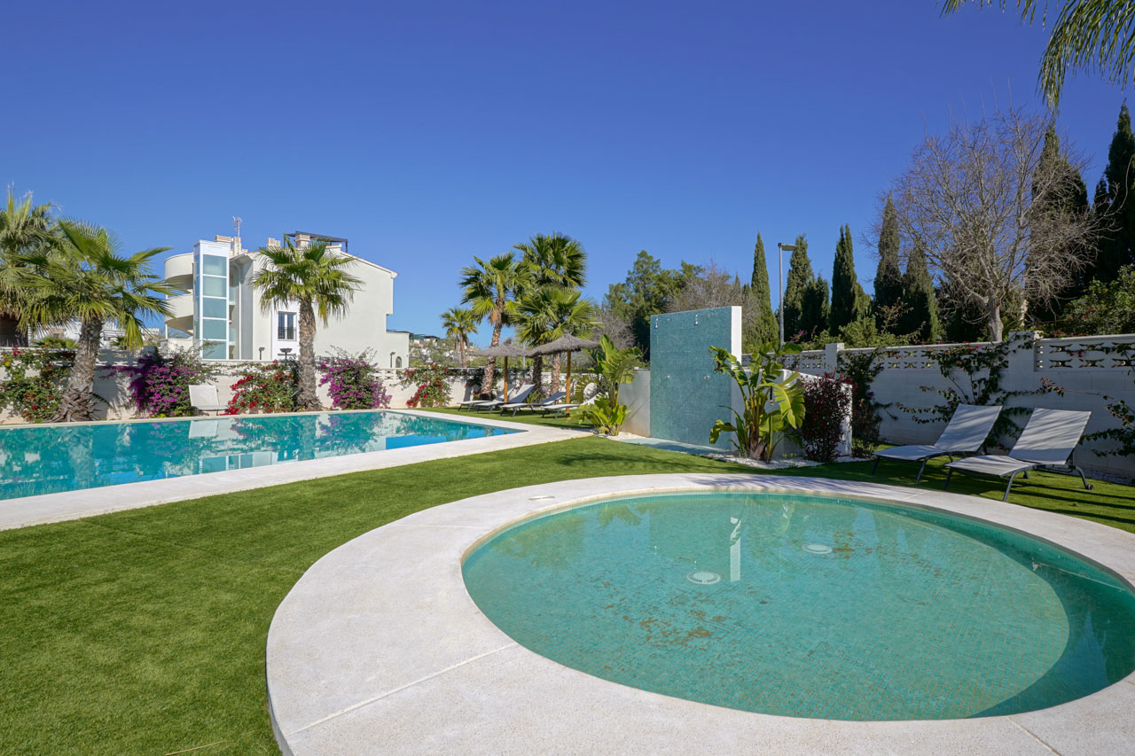 Espace extérieur comprenant une piscine rectangulaire, un bassin circulaire, une douche en mosaïque turquoise et un jardin paysager avec palmiers.