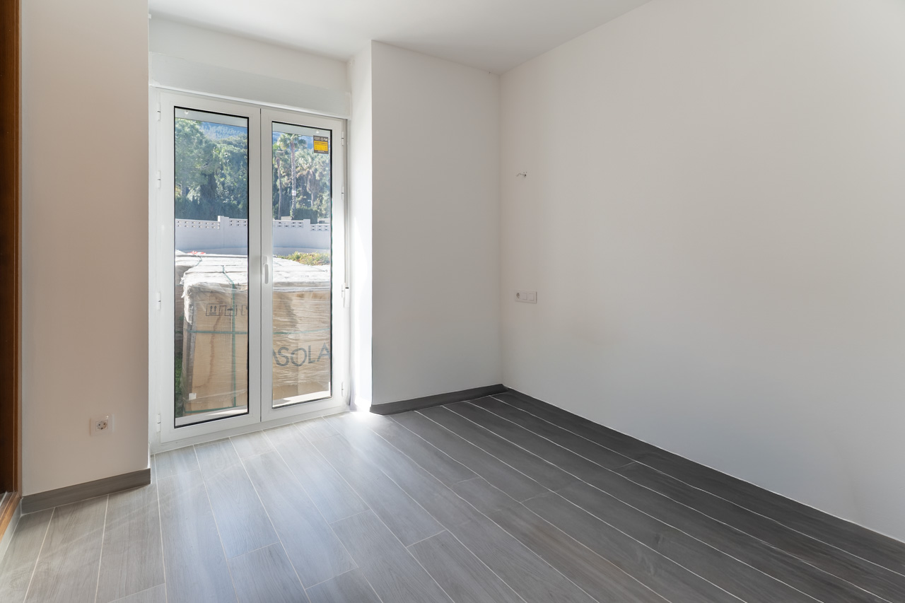 Pièce vide avec sol en grès cérame gris effet bois et porte vitrée en PVC blanc offrant un accès direct à l'extérieur.