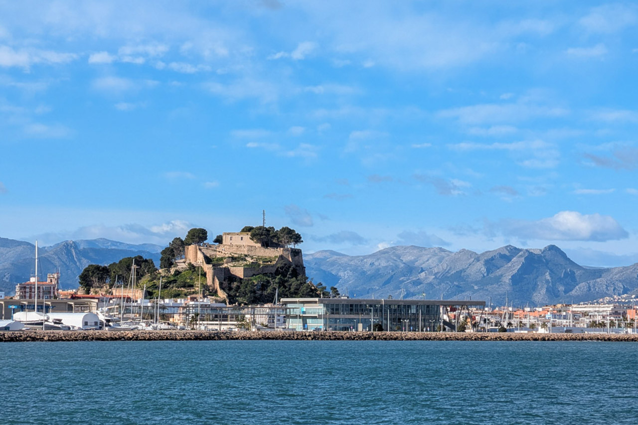 Vue panoramique du château historique sur la colline surplombant le port de plaisance et les montagnes escarpées en arrière-plan.