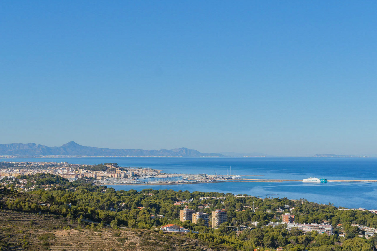 Vue panoramique sur le port et la côte, avec la mer Méditerranée, les montagnes en arrière-plan et une forêt de pins luxuriante.