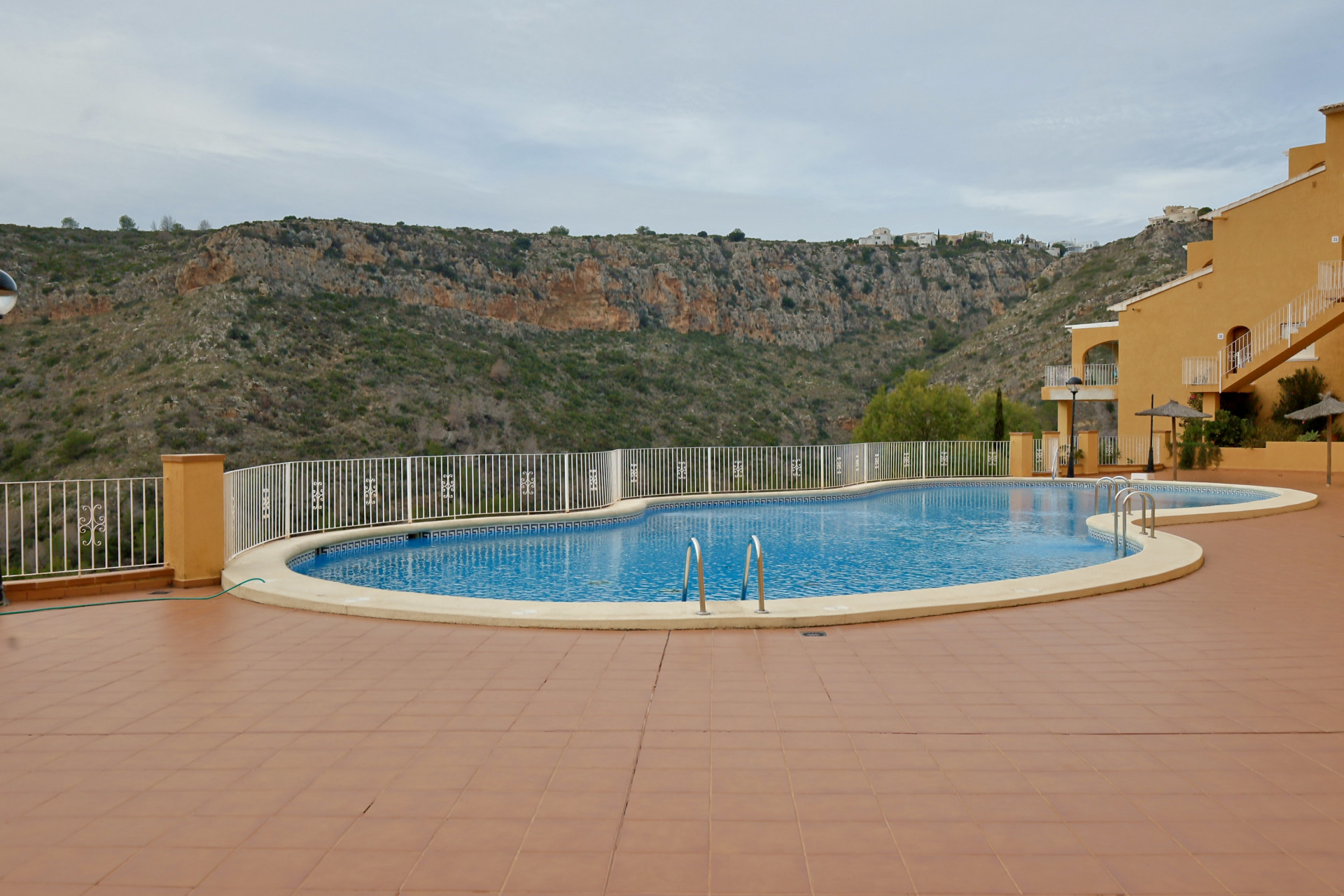 Piscine communautaire aux formes arrondies avec terrasse en terre cuite et garde-corps blanc, offrant une vue sur la vallée rocheuse.