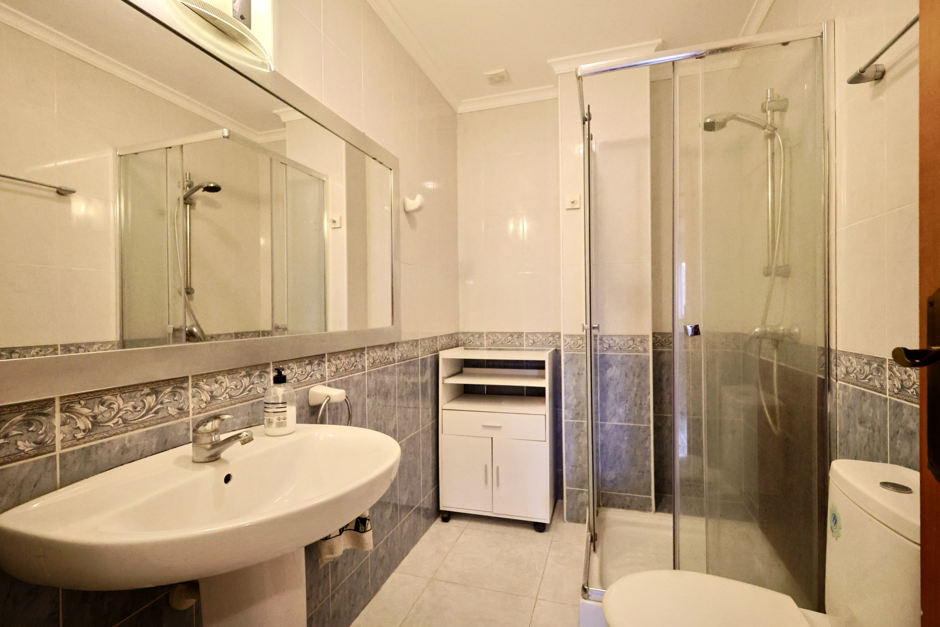 Salle de bain avec douche à paroi vitrée, lavabo sur colonne et carrelage mural bleu agrémenté d'une frise décorative.
