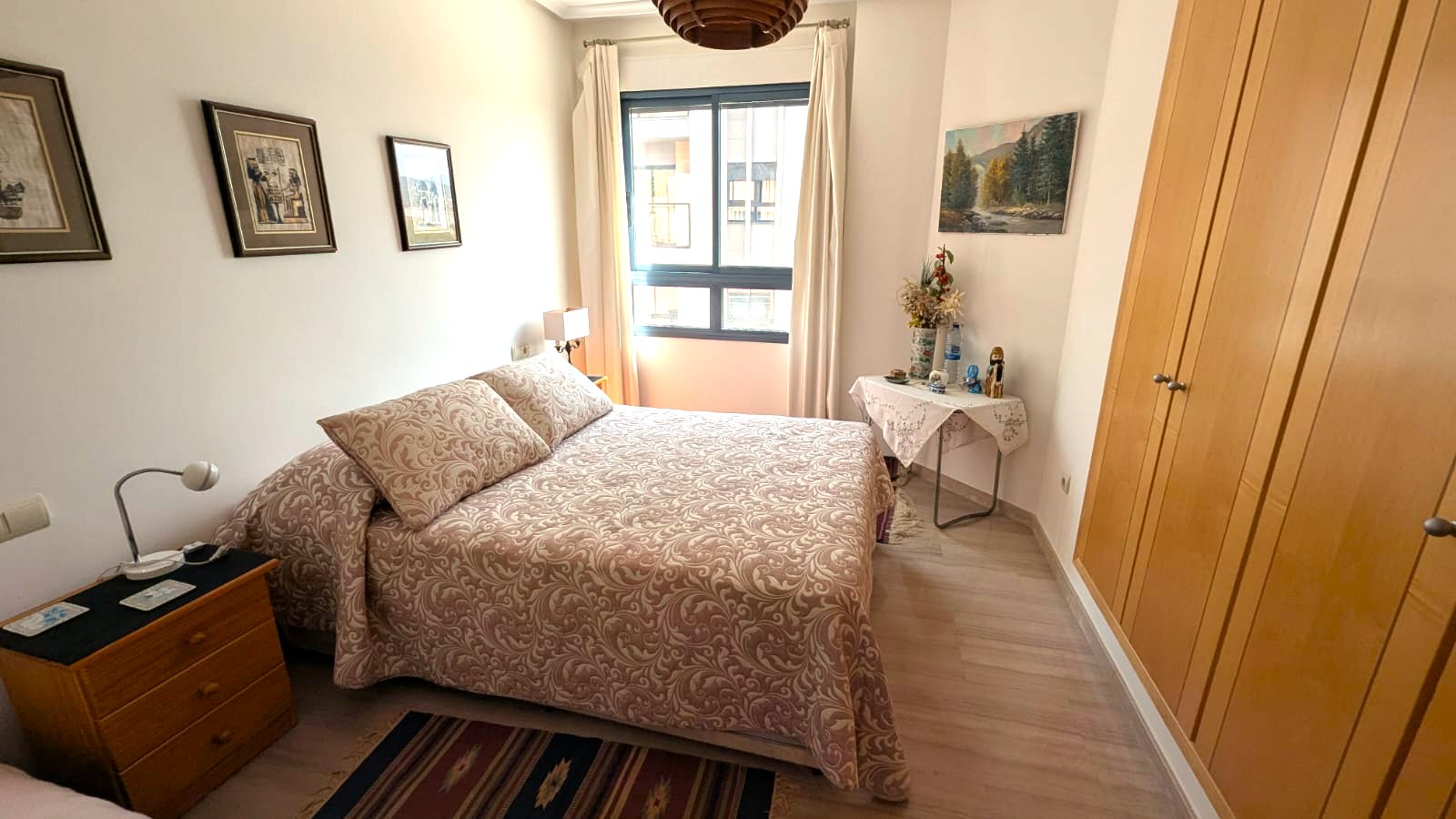 Chambre avec placards intégrés en bois, sol en stratifié clair et fenêtre apportant de la lumière naturelle. Mobilier fonctionnel et décoration classique aux tons chauds.