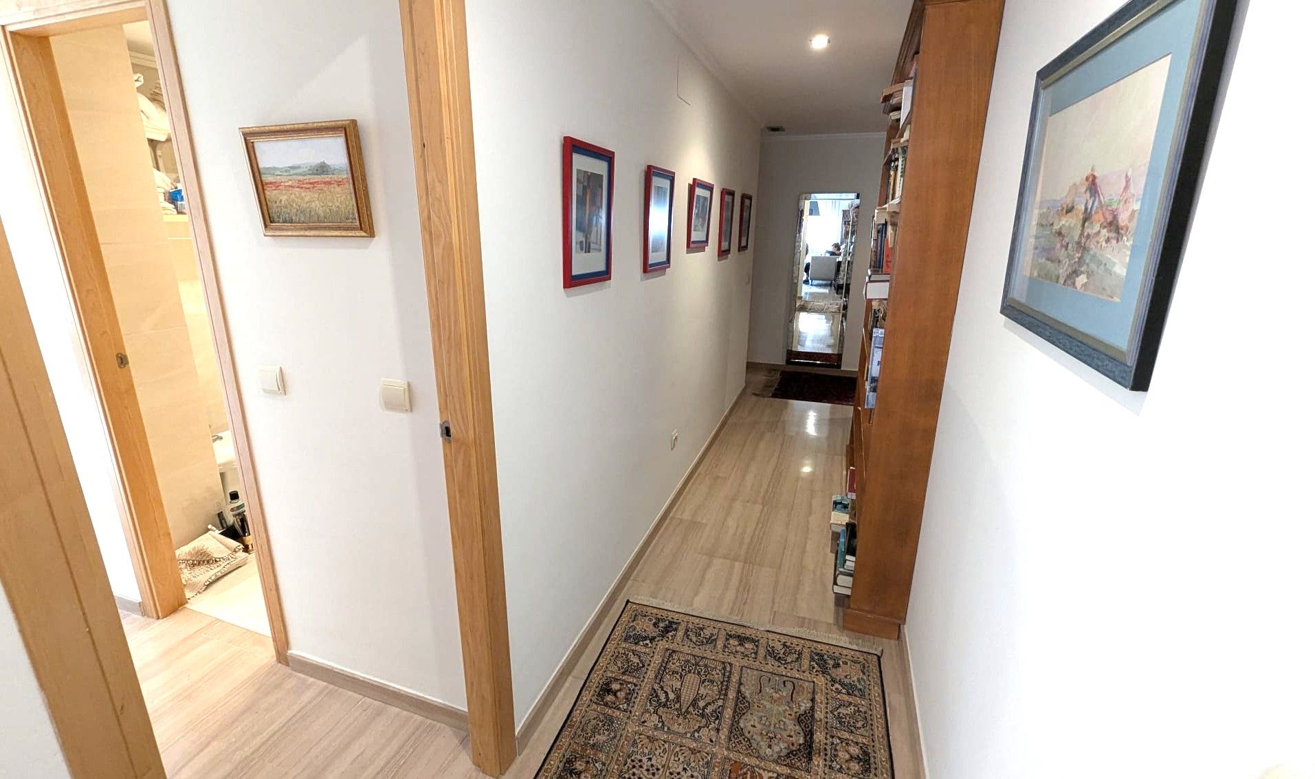 Couloir lumineux avec sol en pierre polie, encadrements de portes en bois et une grande bibliothèque. Décoré d'œuvres d'art et d'un éclairage encastré.