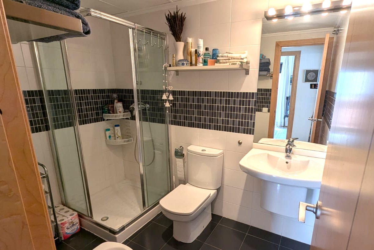 Salle de bains avec cabine de douche vitrée, carrelage mural blanc agrémenté d'une frise en mosaïque sombre et sol en grès gris.