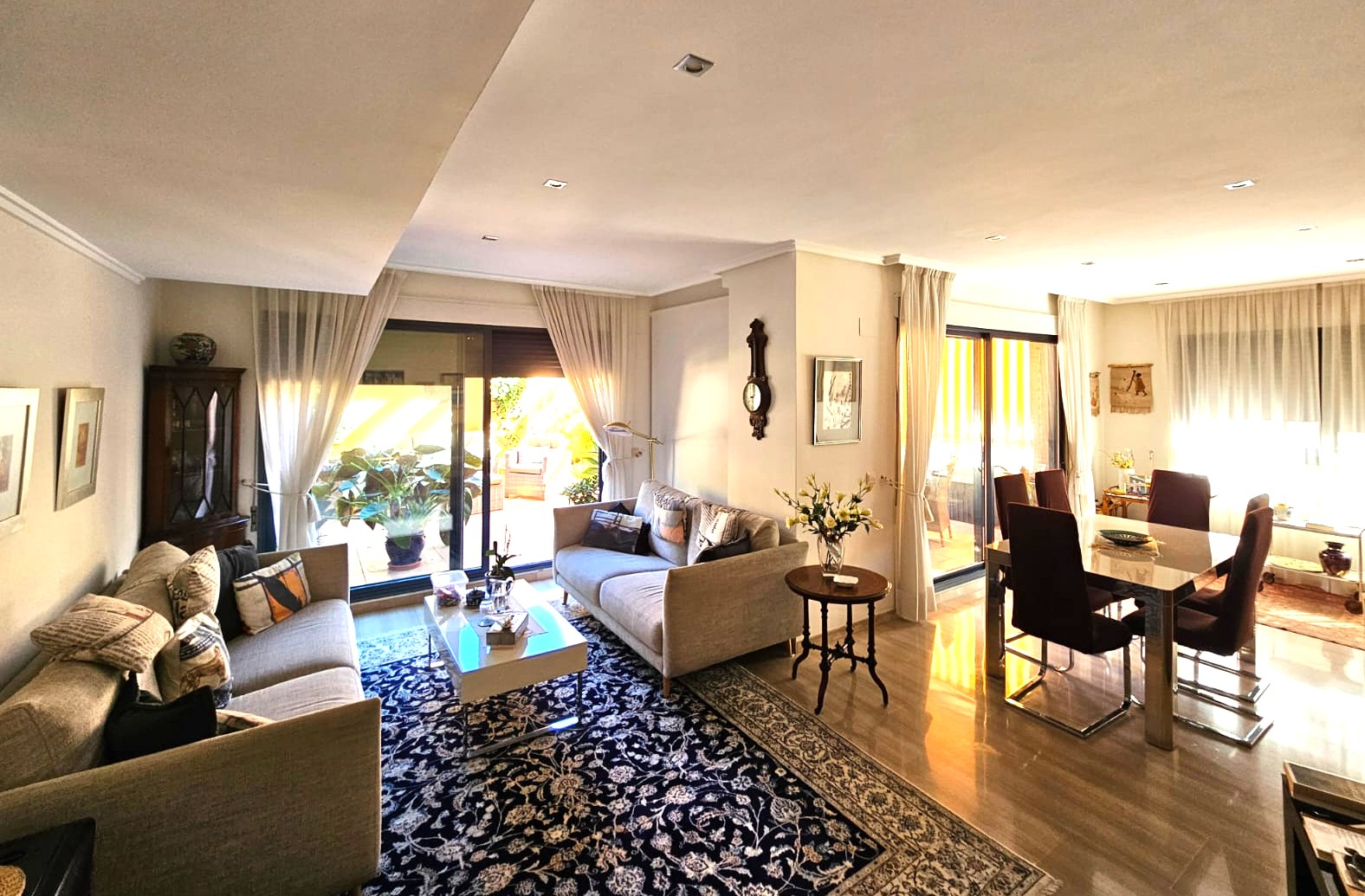 Séjour ouvert avec salle à manger, sols en pierre polie et éclairage encastré, offrant un accès direct à une terrasse privée par de larges baies vitrées.