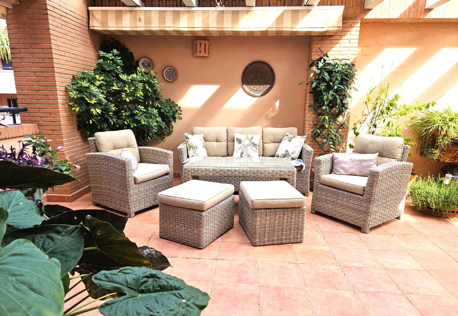 Terrasse privée avec sol en terre cuite, salon de jardin en résine tressée et auvent rétractable, entourée de plantes et de piliers en briques.