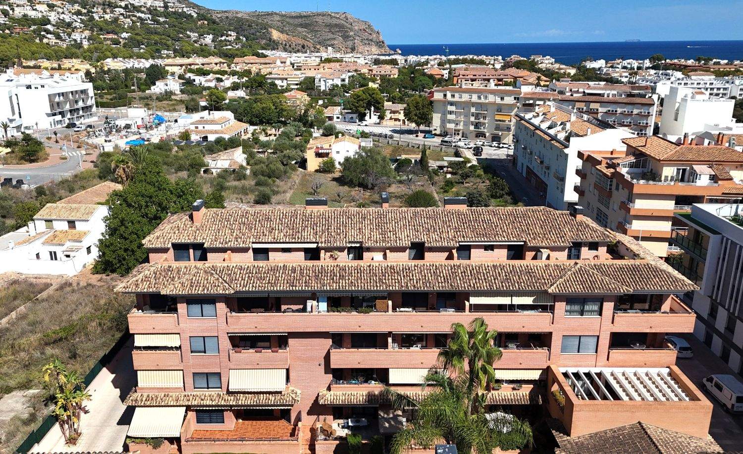 Vue aérienne d'un immeuble en briques avec toits en terre cuite, balcons équipés de stores, offrant une perspective sur la ville de Jávea et la mer Méditerranée.