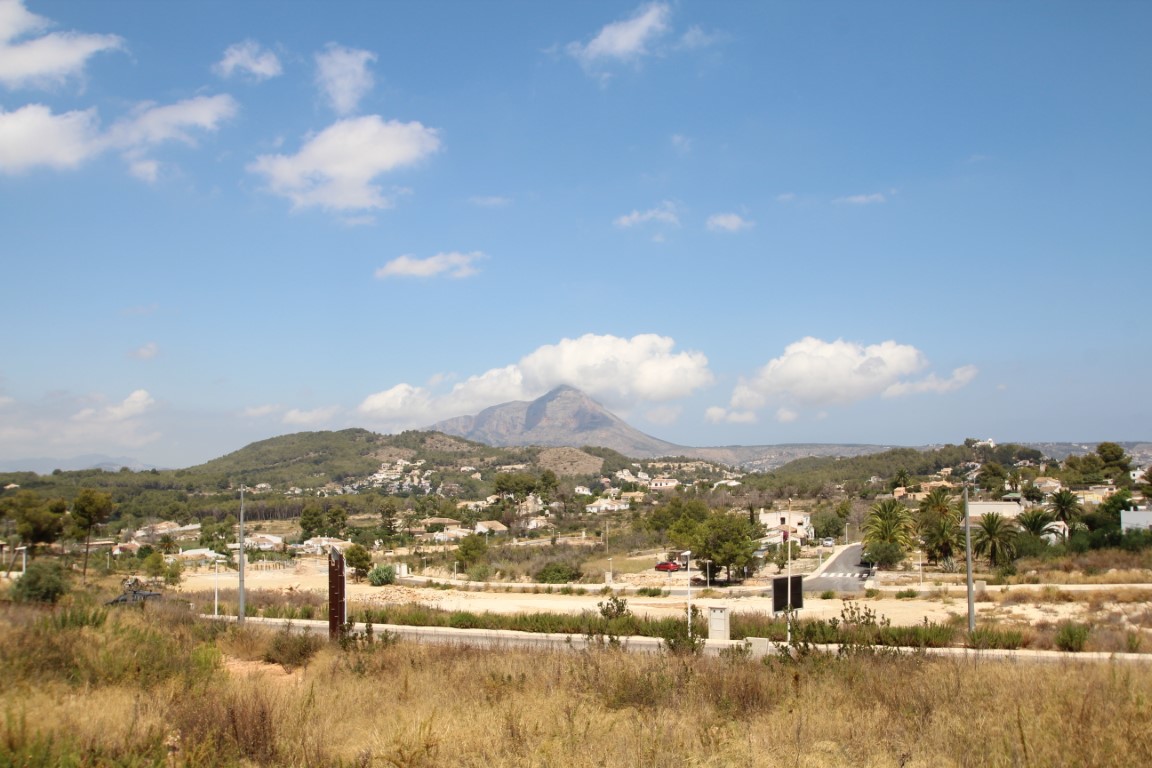 Vue sur des terrains à bâtir avec le Montgó en arrière-plan, sous un ciel bleu avec des nuages dispersés.