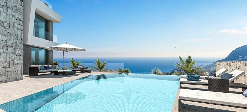 Vue sur la piscine à débordement carrelée de bleu et les chaises longues avec vue sur la mer.