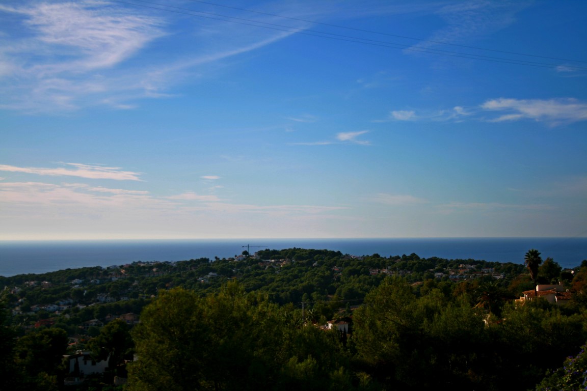Vue panoramique de Benimeit, Moraira, avec la mer Méditerranée en arrière-plan et un ciel bleu nuageux.