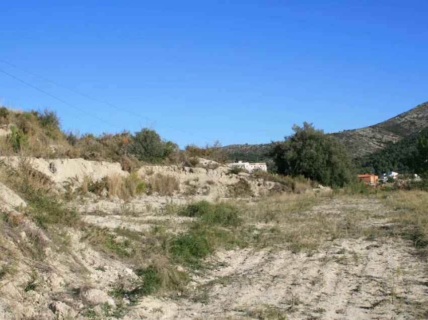 Vue du terrain avec végétation indigène et collines en arrière-plan, sous un ciel bleu dégagé.