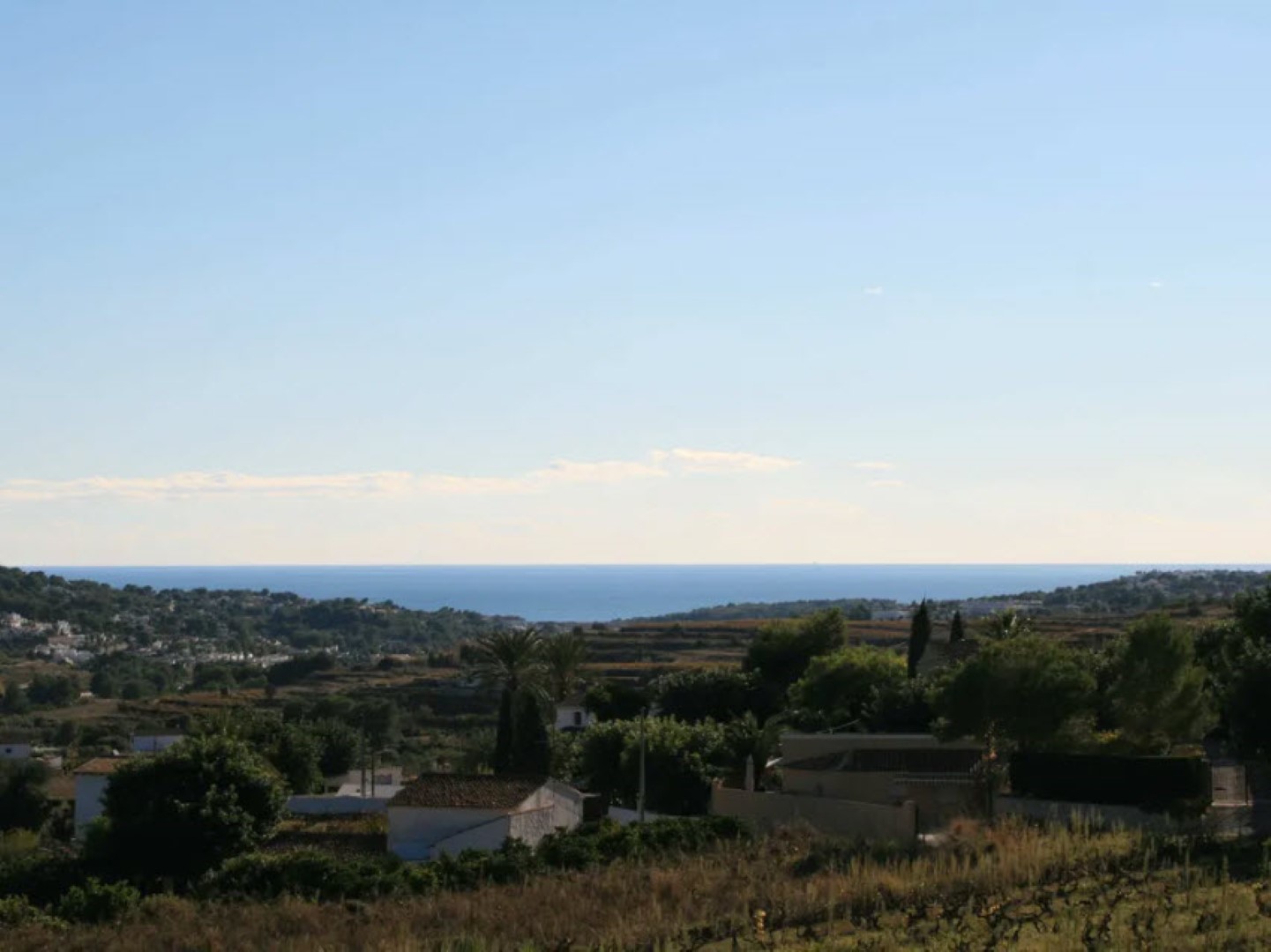 Vue panoramique du terrain avec des maisons aux toits de tuiles et la Méditerranée en arrière-plan sous un ciel bleu clair.