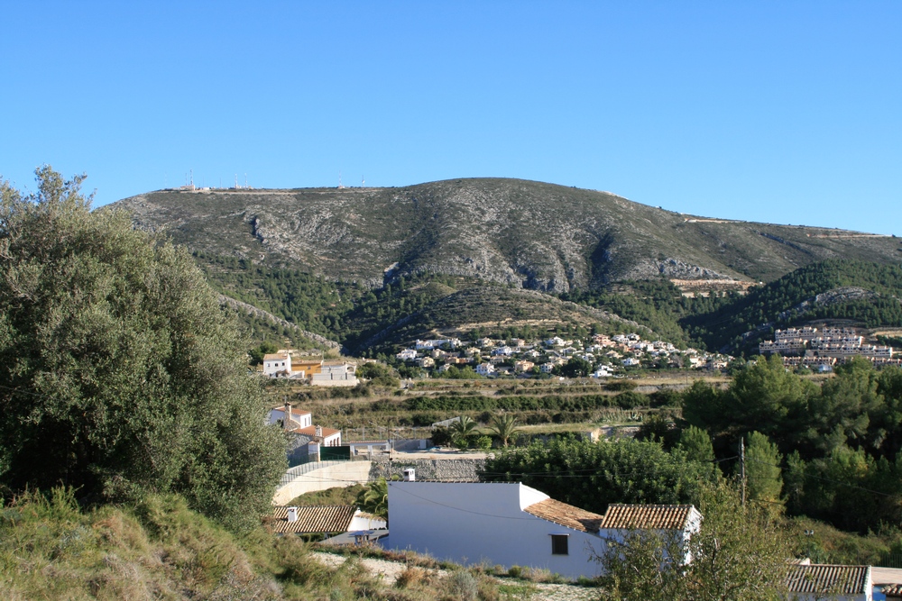 Vue sur le paysage rural de Benitachell avec des maisons aux toits de tuiles et une montagne en arrière-plan.