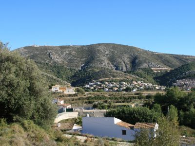 Vue sur le paysage rural de Benitachell avec des maisons aux toits de tuiles et une montagne en arrière-plan.