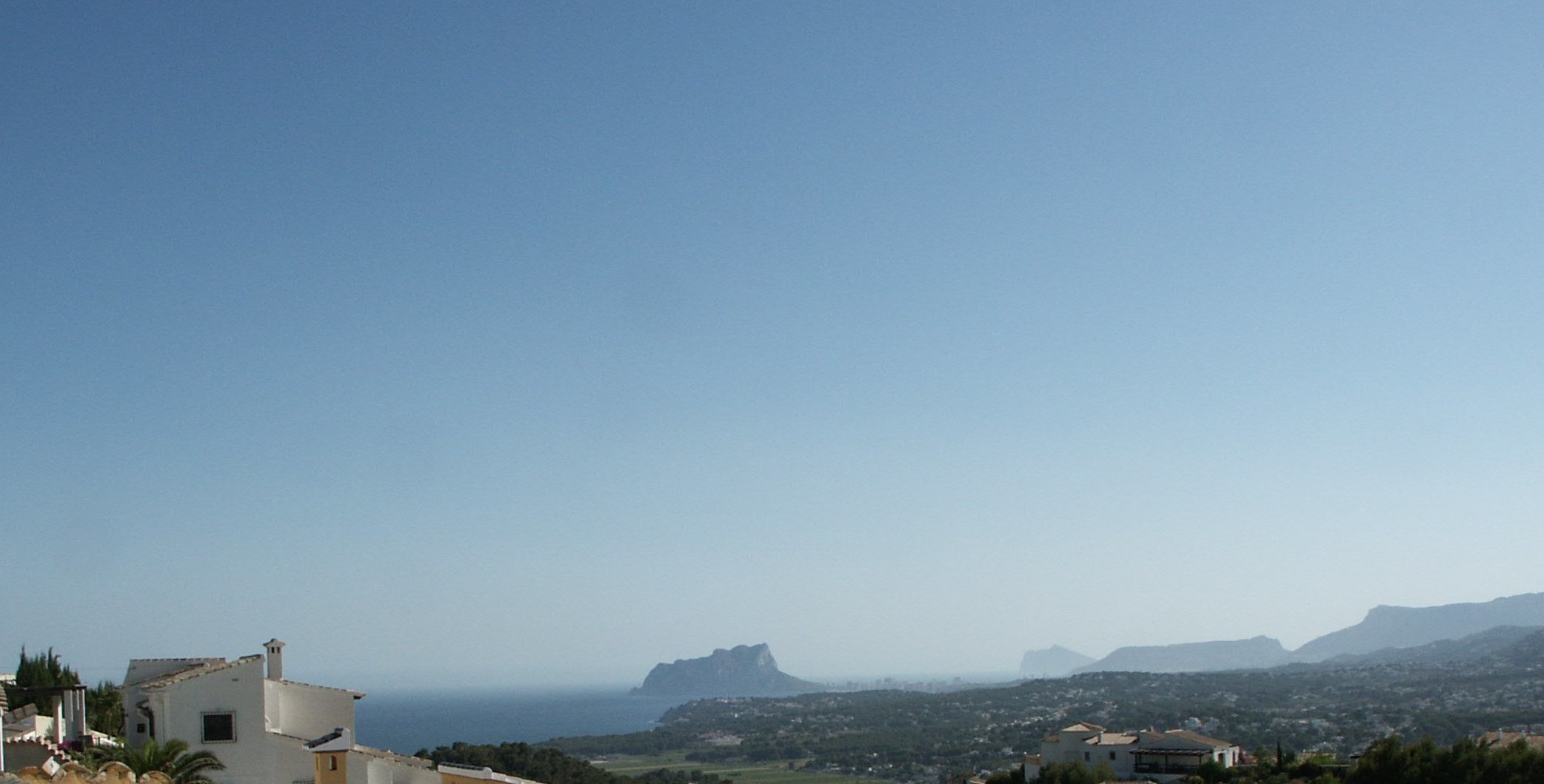 Vue panoramique de Benitachell avec le Peñón de Ifach en arrière-plan, sous un ciel dégagé.