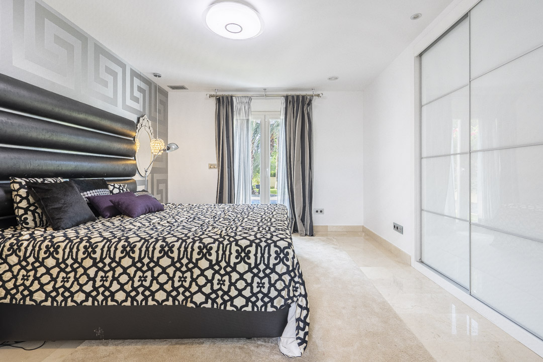 Chambre avec grand placard intégré aux portes coulissantes blanches, sol en marbre poli et accès direct au jardin par des portes-fenêtres.