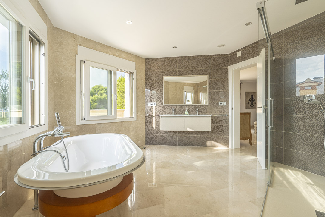 Salle de bain spacieuse avec baignoire îlot sur socle en bois, double vasque et douche à l'italienne. Les finitions incluent du marbre et des carreaux muraux à motifs élégants.