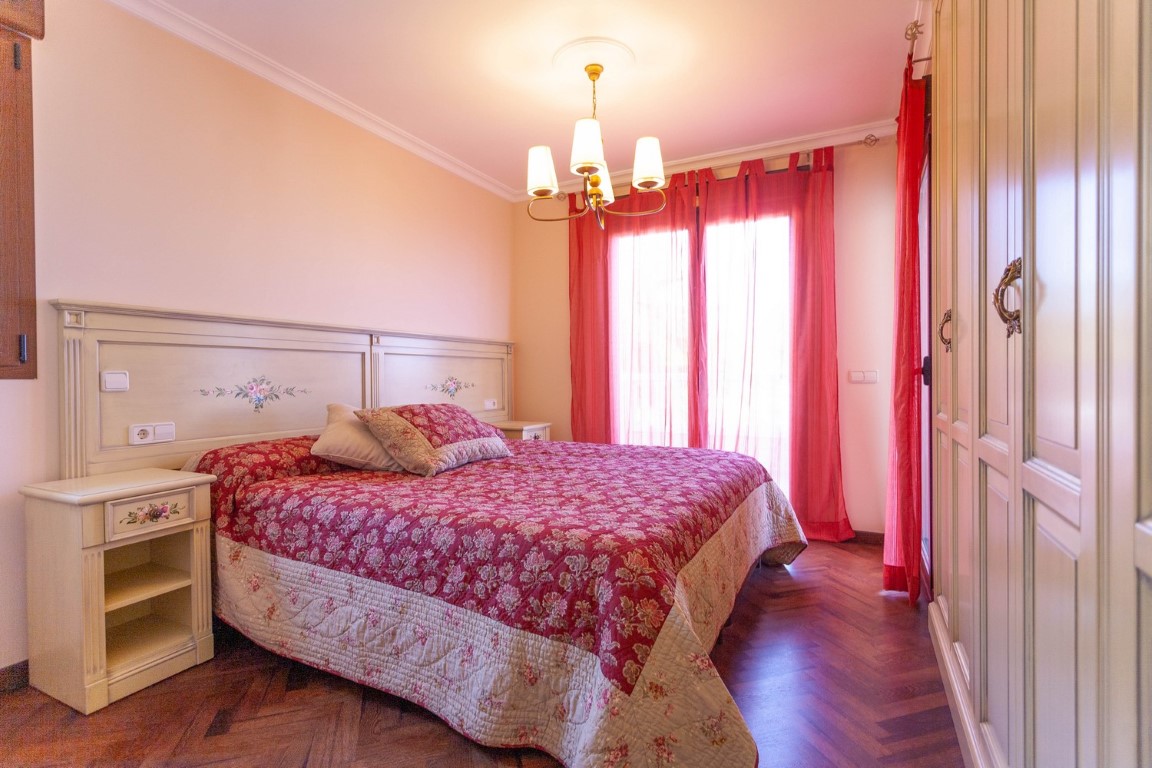 Chambre avec parquet en chevrons, armoires encastrées crème et accès au balcon. Comprend un mobilier classique aux motifs floraux et des rideaux rouges.