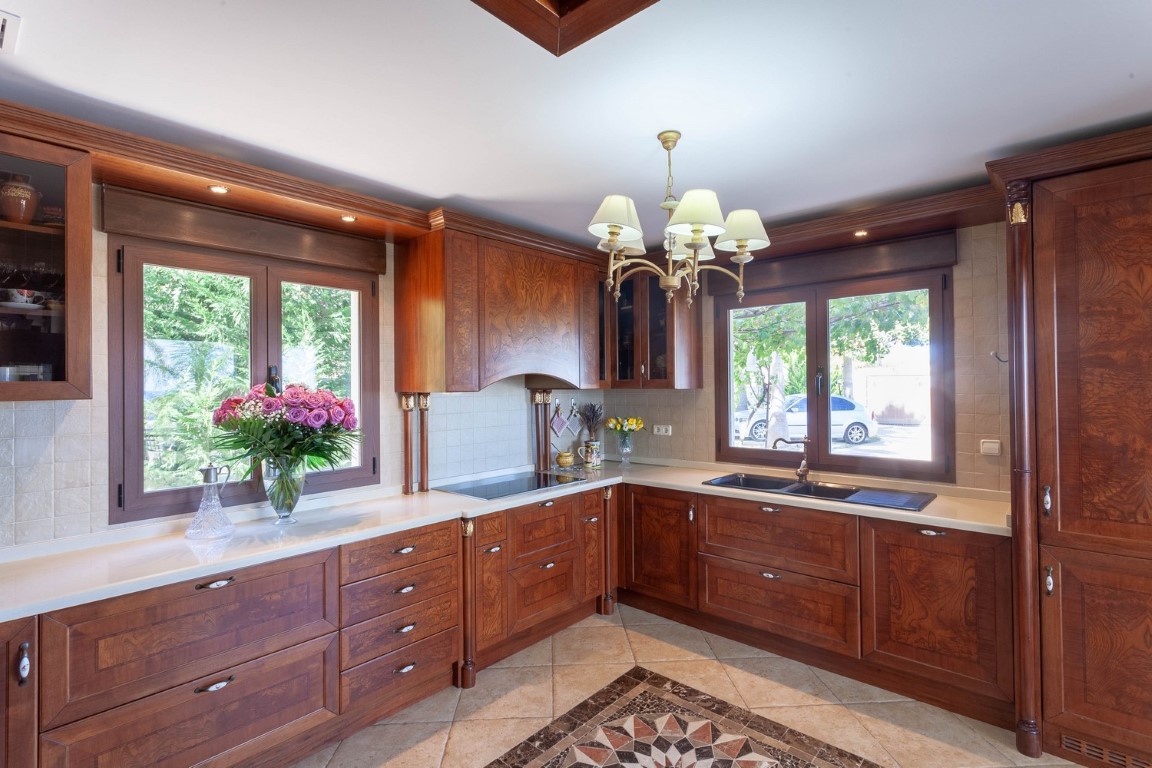 Cuisine classique avec des meubles en bois massif, un plan de travail clair, un sol carrelé avec mosaïque et de grandes fenêtres lumineuses.