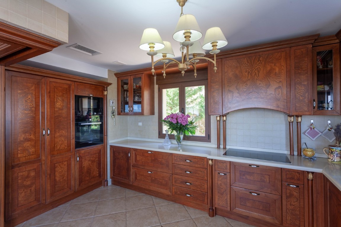 Cuisine de style classique avec des armoires en bois, un plan de travail blanc et des appareils intégrés. Elle dispose d'une plaque à induction et d'un lustre élégant.