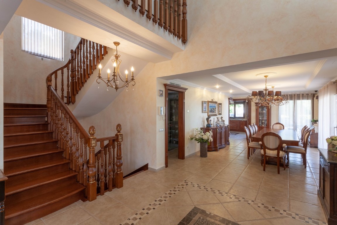 Hall d'entrée spacieux avec escalier en bois sculpté et sol en céramique décorée, s'ouvrant sur une salle à manger formelle au style classique.