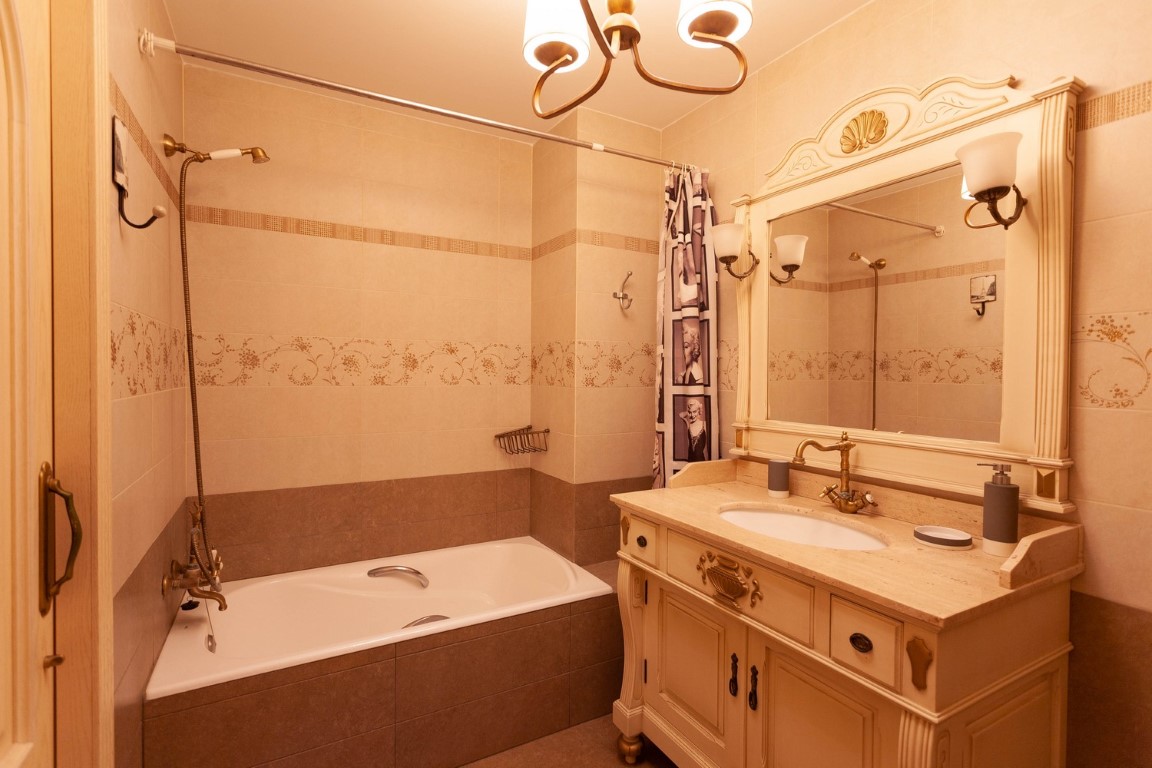 Salle de bain de style classique avec meuble vasque en bois sculpté, plan en pierre et robinetterie en bronze. Comprend une baignoire encastrée et un carrelage décoratif.