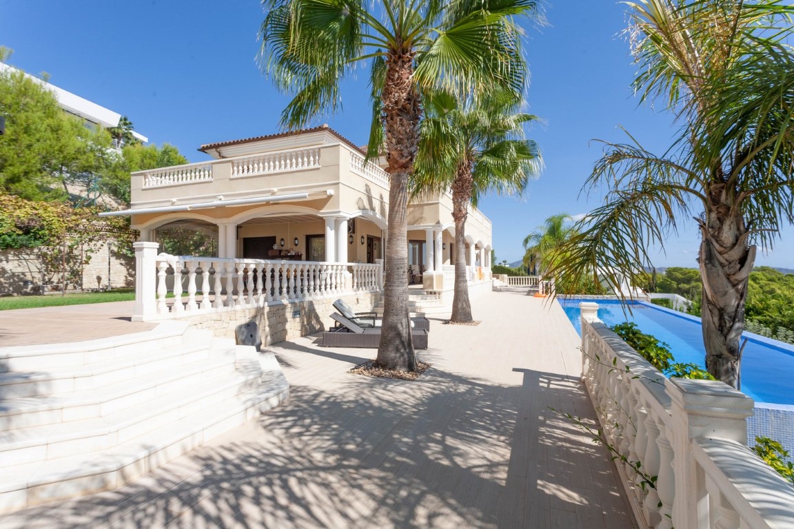 Terrasse extérieure avec balustrades classiques, palmiers et piscine à débordement longeant la villa méditerranéenne aux arcades élégantes.