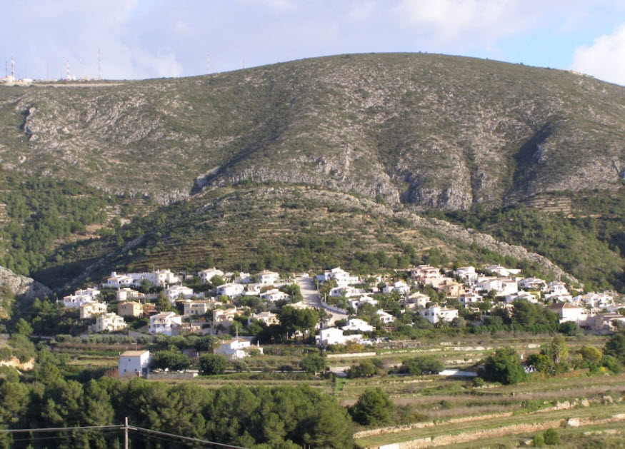 Vue panoramique d'une colline en terrasses à Benitachell, présentant des villas blanches intégrées dans un paysage montagneux avec une végétation méditerranéenne.