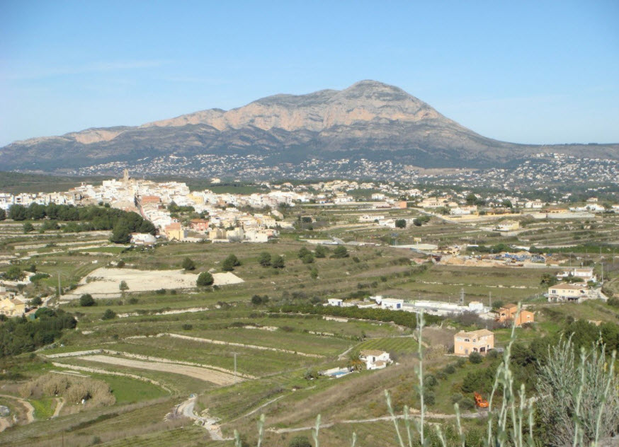 Vue panoramique sur le terrain en restanques à Benitachell, avec le massif du Montgó en arrière-plan et le village typique environnant.