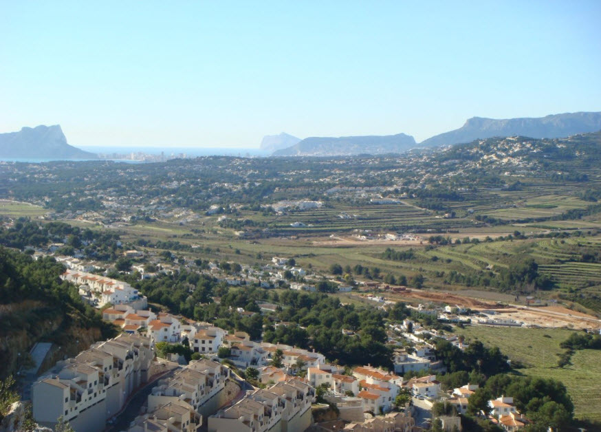 Vue panoramique surélevée sur la vallée de Benitachell vers la mer Méditerranée, montrant les paysages en terrasses et les formations rocheuses côtières au loin.
