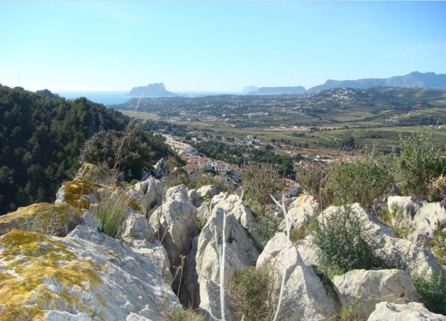 Vues panoramiques depuis le terrain surélevé vers le Peñón de Ifach et la mer Méditerranée, avec des formations rocheuses naturelles et la flore locale.