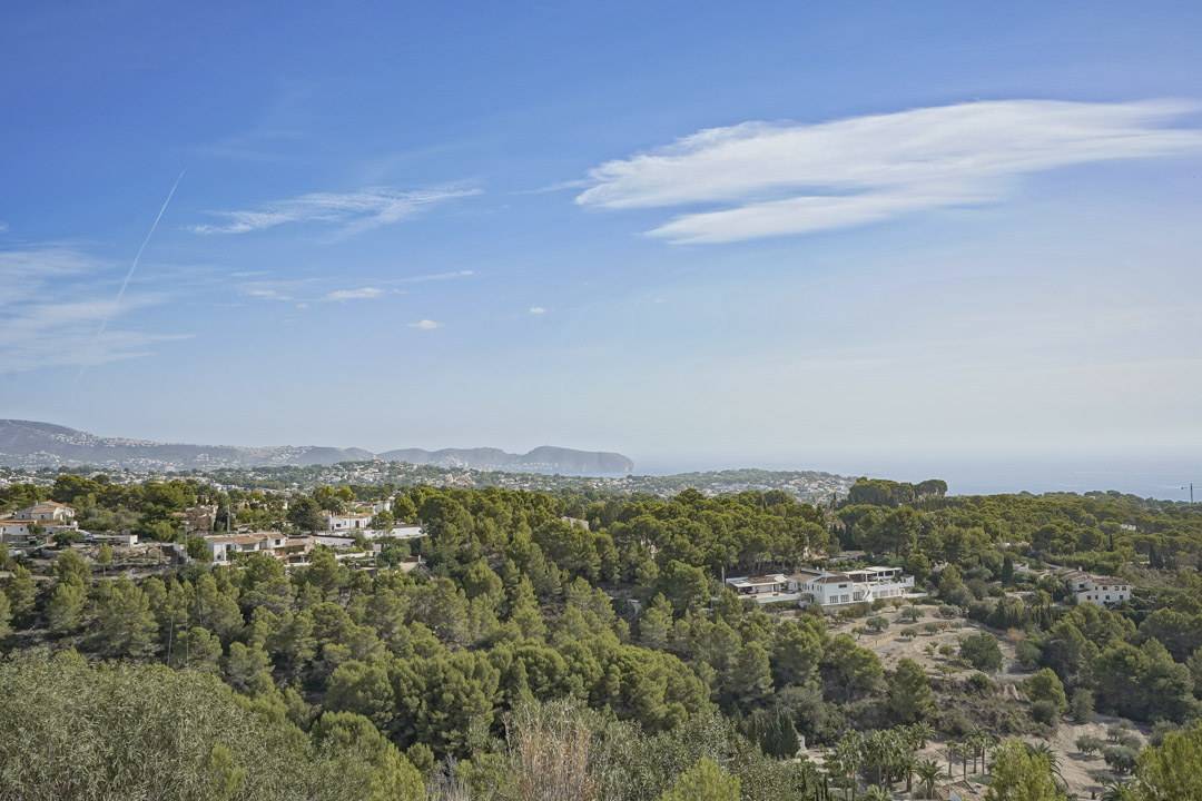 Vue panoramique depuis le terrain surplombant une pinède méditerranéenne, des villas résidentielles et l'horizon marin sous un ciel dégagé.