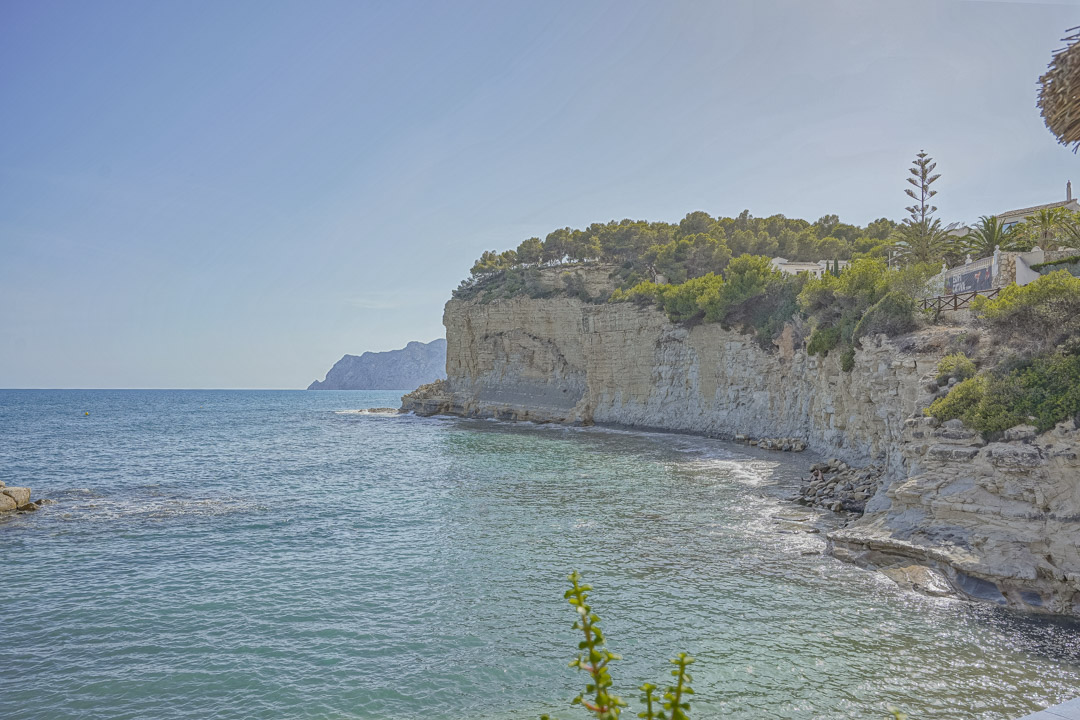 Vue panoramique sur les falaises de calcaire et les eaux turquoises près de la plage de La Fustera, bordées de pins parasols et de côtes rocheuses.