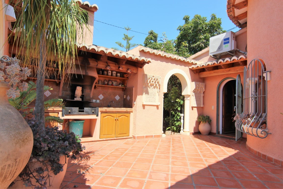 Terrasse extérieure avec cuisine d'été, barbecue intégré et sol en terre cuite. On y trouve une arche décorative méditerranéenne et un porche en bois.